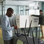 Dois homens preparam cabines de votação em uma seção eleitoral.