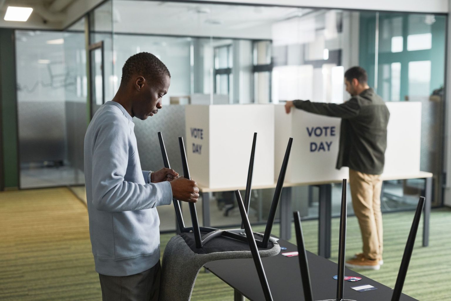 Dois homens preparam cabines de votação em uma seção eleitoral.