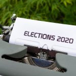 Máquina de escrever com uma folha exibindo a palavra “Elections 2020”, em ambiente externo.