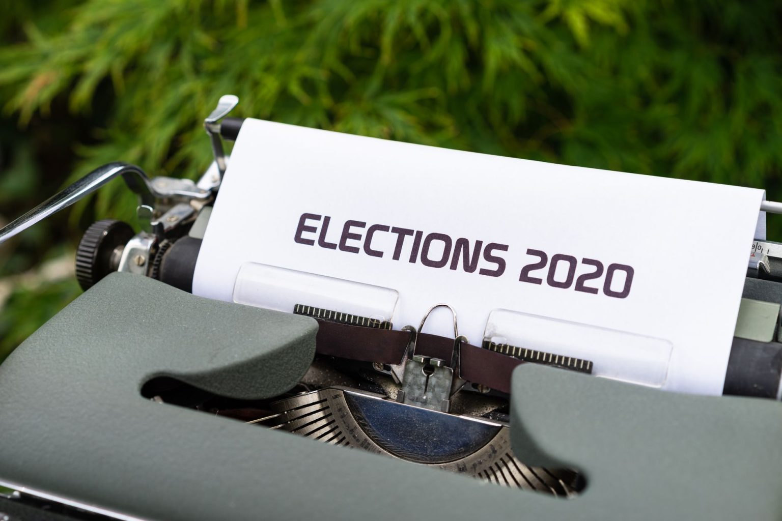 Máquina de escrever com uma folha exibindo a palavra “Elections 2020”, em ambiente externo.