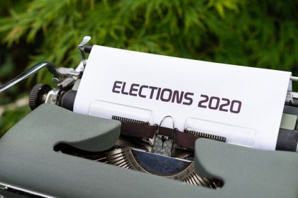 Máquina de escrever com uma folha exibindo a palavra “Elections 2020”, em ambiente externo.