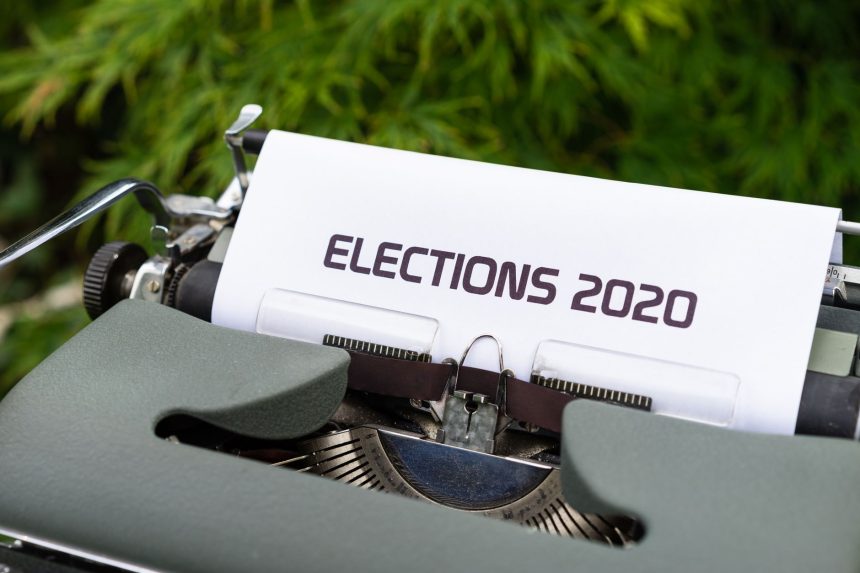 Máquina de escrever com uma folha exibindo a palavra “Elections 2020”, em ambiente externo.