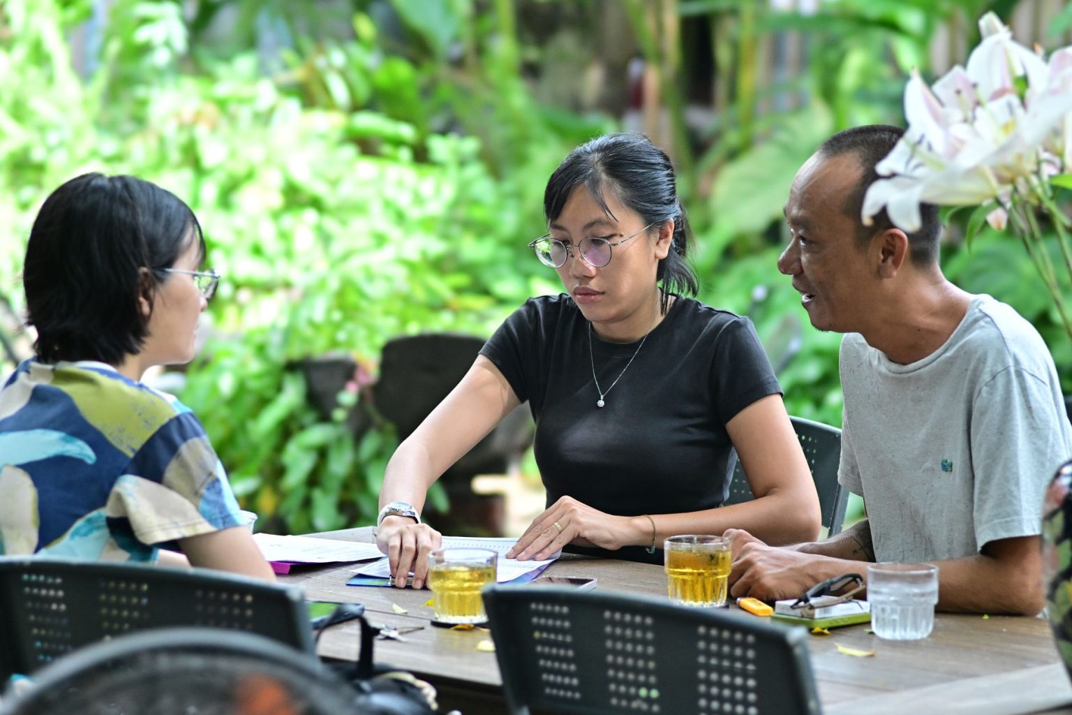 Grupo de adultos reunido em torno de uma mesa, participando de uma discussão em um ambiente arborizado.
