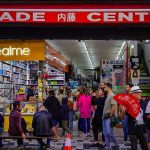 Consumidores circulam por um centro comercial movimentado, entre bancas e lojas.