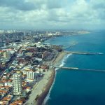 Vista aérea da orla de Fortaleza, com a faixa de praia, o mar e a área urbana da cidade
