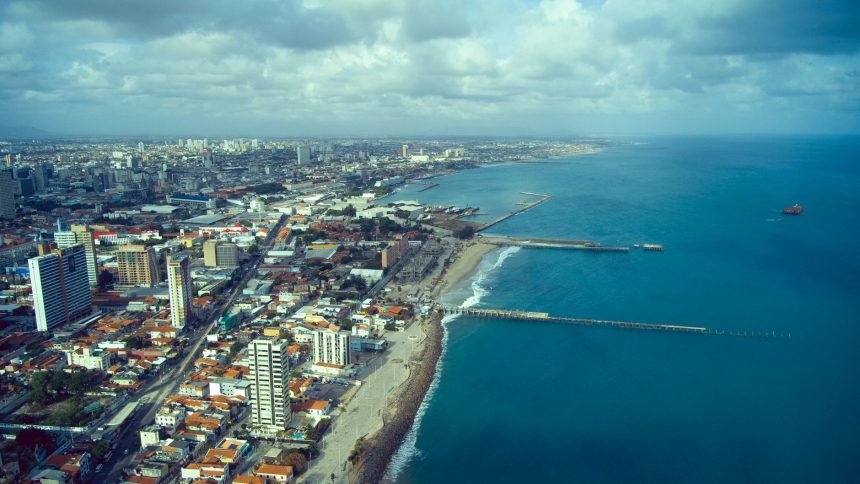 Vista aérea da orla de Fortaleza, com a faixa de praia, o mar e a área urbana da cidade